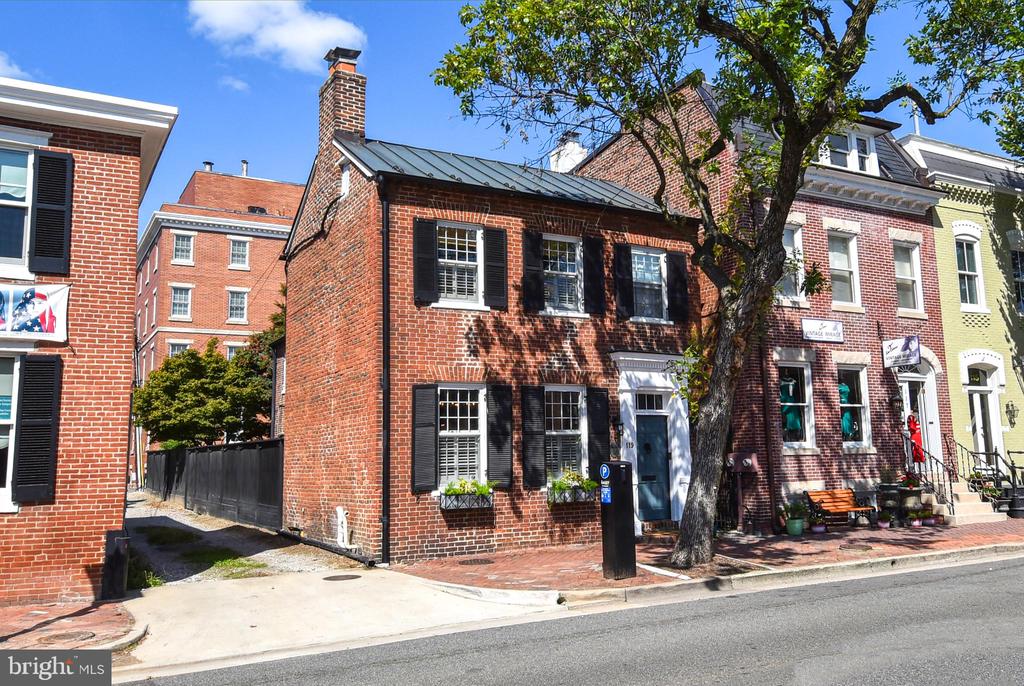 Red-brick rowhouse with black shutters and a blue door beneath a leafy street tree.