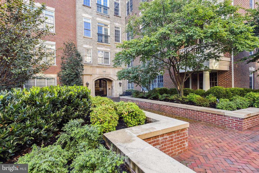 Brick apartment building entrance with an arched doorway and landscaped courtyard.