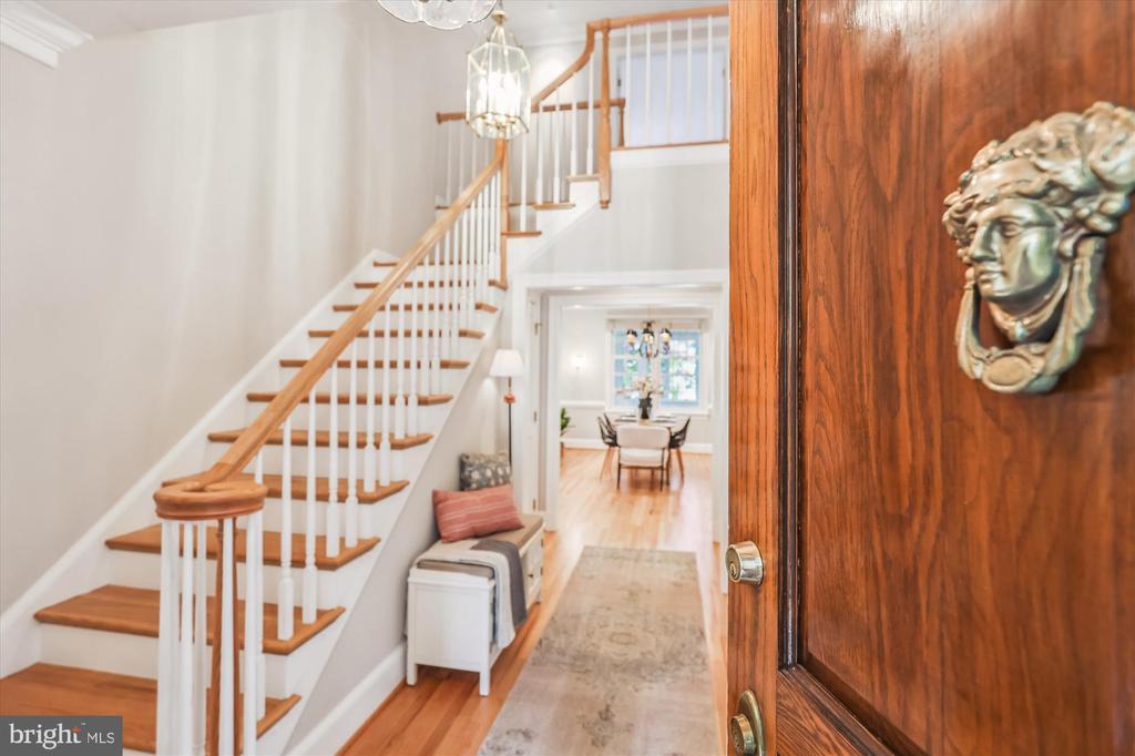Entryway with a wood-and-white staircase, an open front door, and a sculpted face knocker.