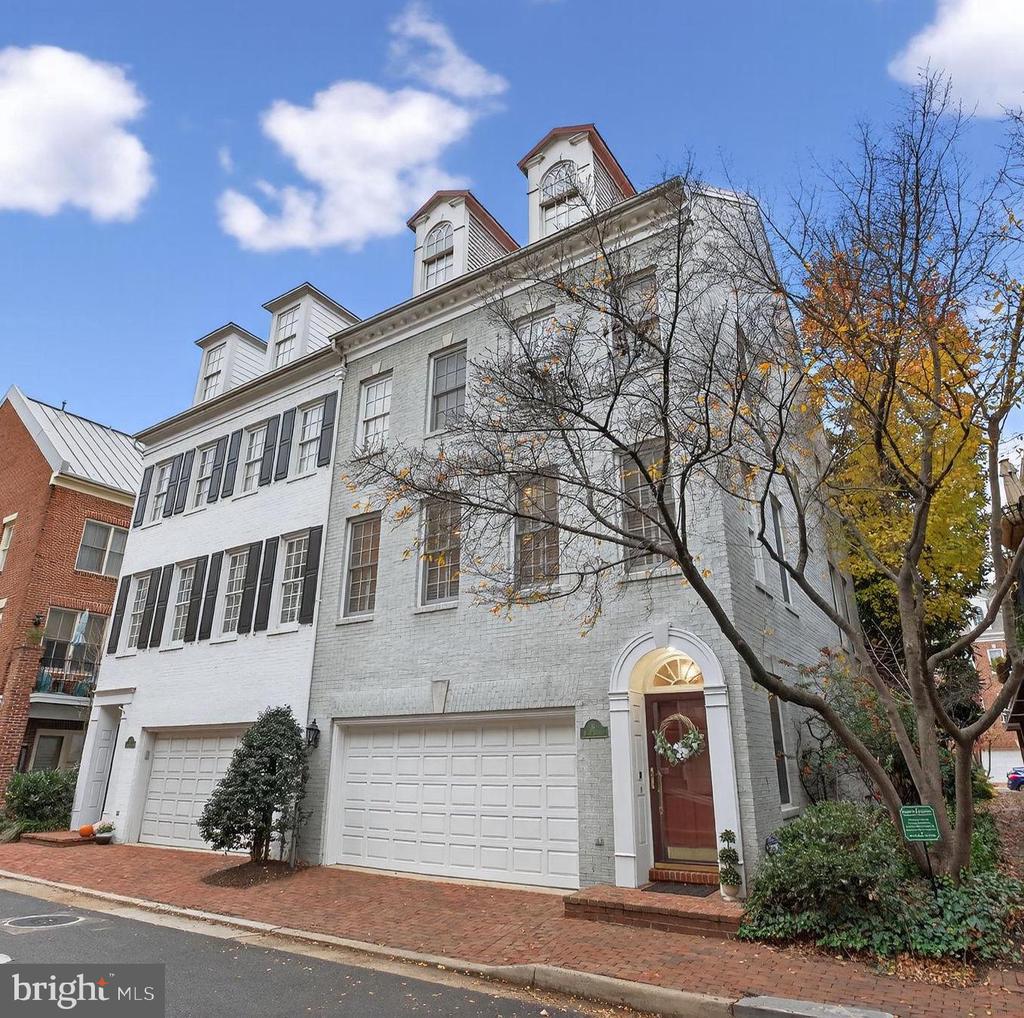 White brick residence with roof dormers, two garage doors, and an arched red-door entry.