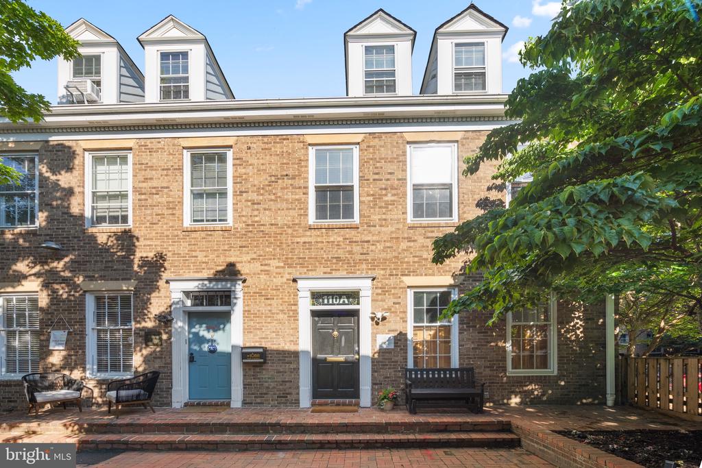 Brick townhouse with dormer windows, two front doors, brick steps, and leafy trees.