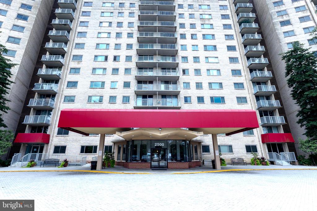 Apartment building with rows of balconies and a wide red canopy over the entrance.