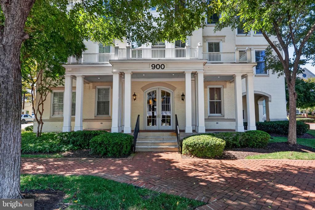 White residential building with a columned entrance, balconies, and brick walkway.