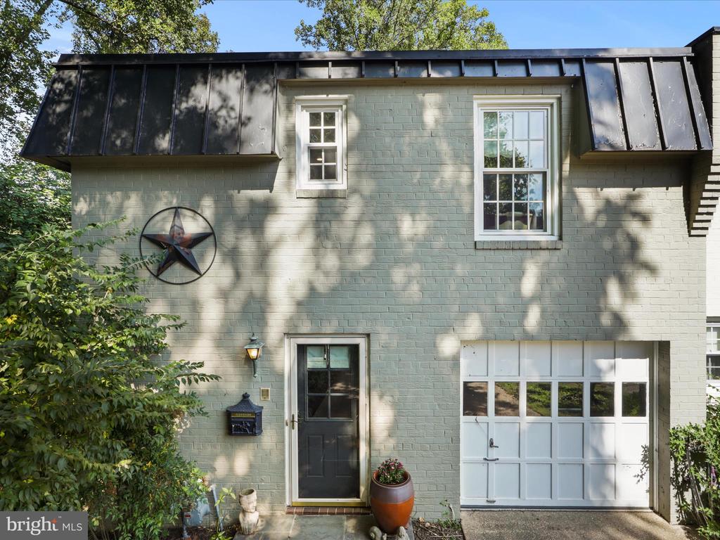 Pale green brick house with a dark metal roof, star wall decoration, and white garage door.
