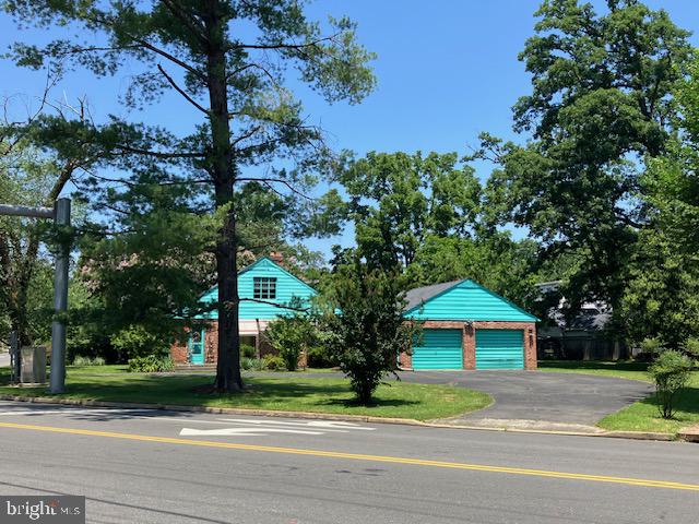Turquoise house and detached garage with brick accents, framed by mature trees.