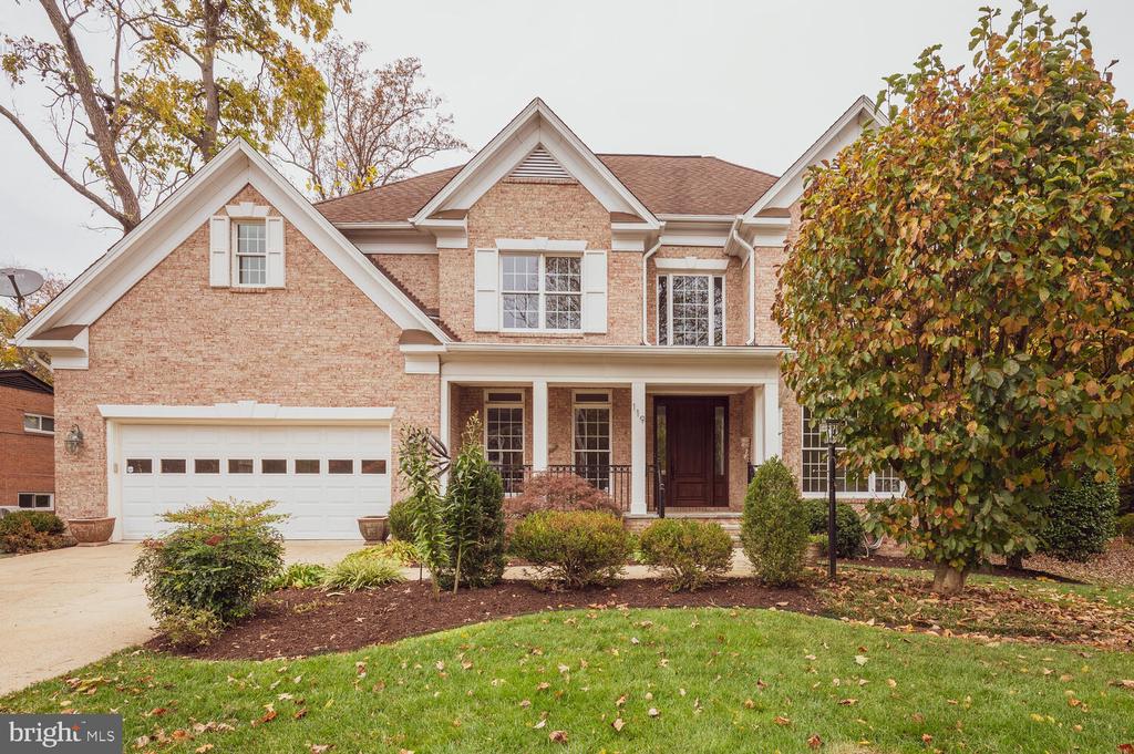 Two-story brick house with a white double garage, covered porch, and autumn trees.