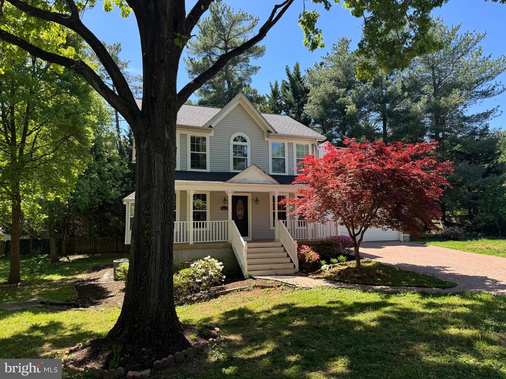Two-story house with a covered porch, framed by a large tree and red-leaf Japanese maple.