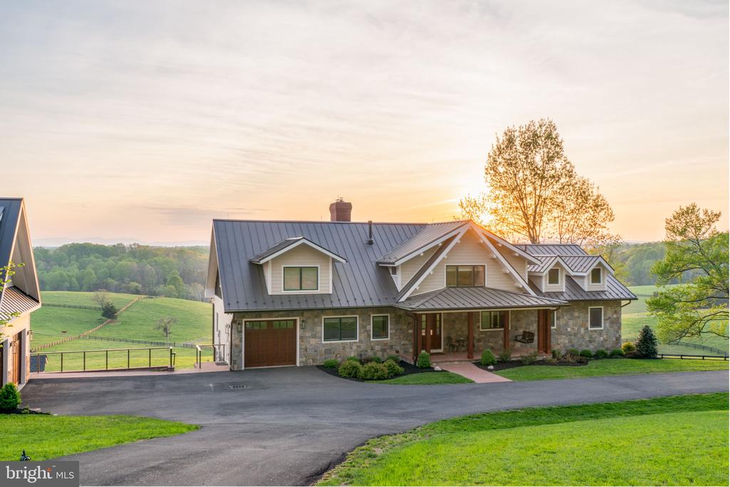 Country home with a metal roof and stone facade overlooking green rolling fields at sunset.