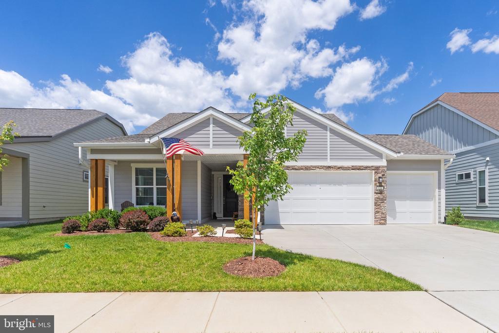 Gray single-story home with a covered porch, American flag, double garage, and landscaped front lawn.