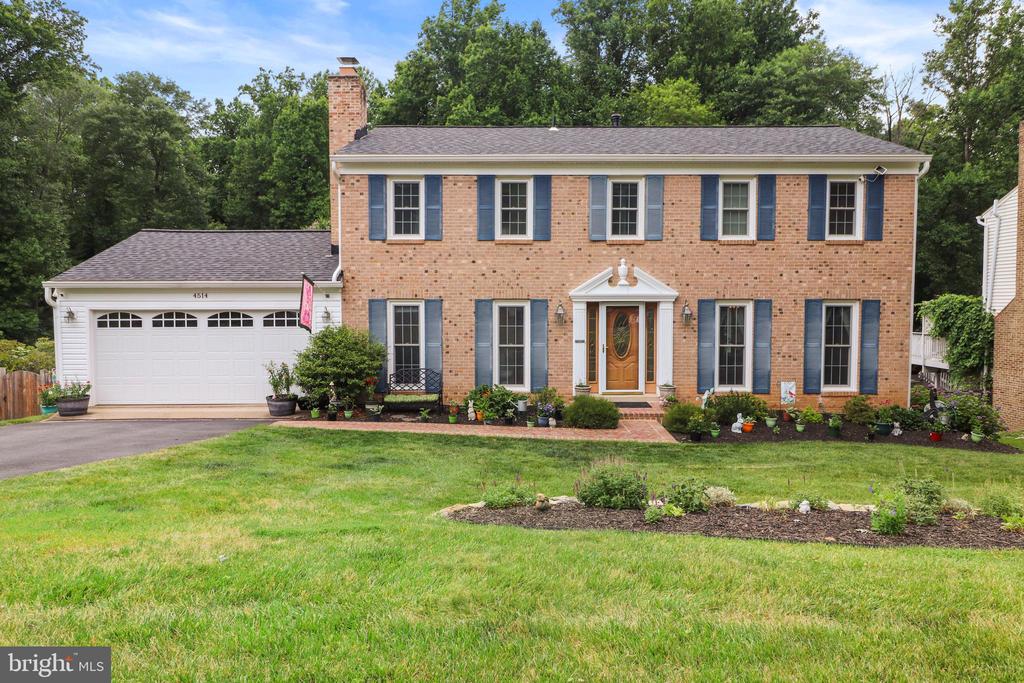 Two-story brick home with blue shutters, an attached garage, and a landscaped front lawn.
