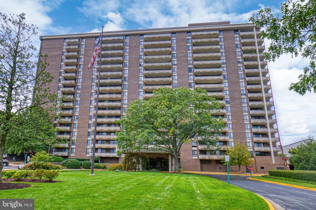 Brick apartment building with rows of balconies, a landscaped lawn, and an American flag.