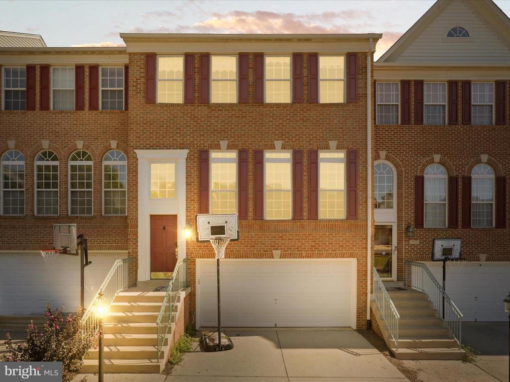 Brick townhouse with red shutters, a double garage, front steps, and a basketball hoop at golden hour.