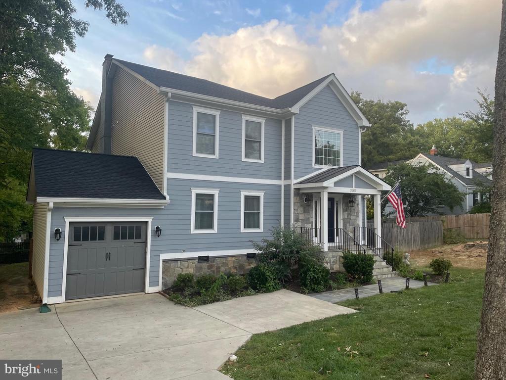 Two-story blue-gray house with an attached garage, stone entry, and American flag.