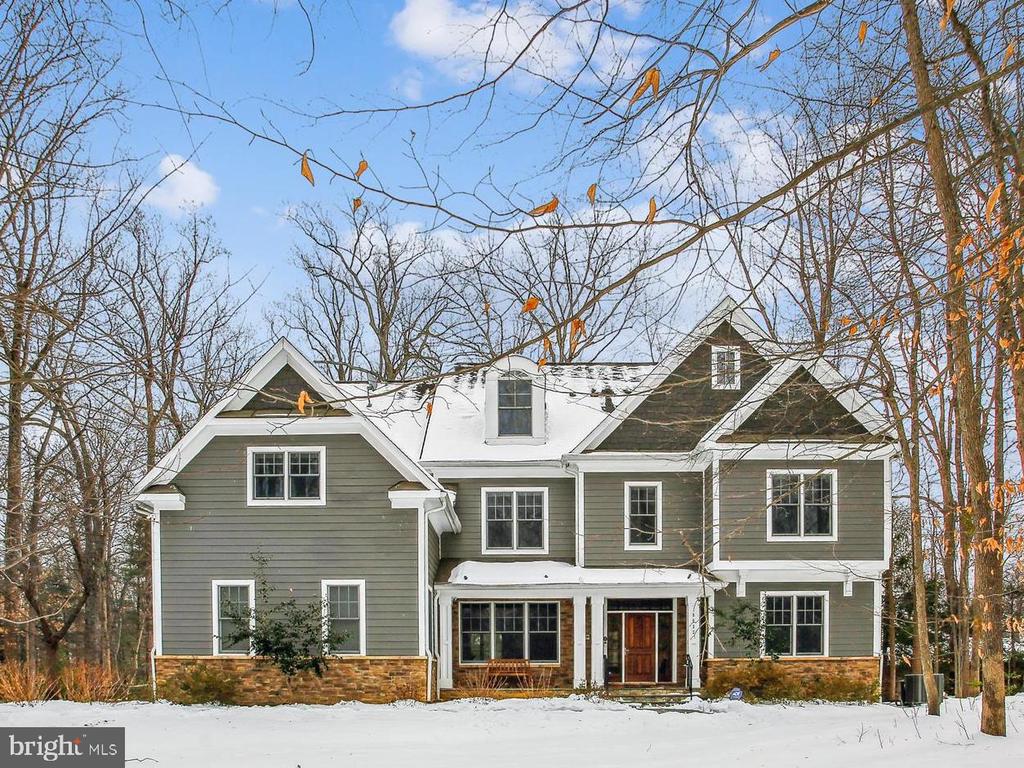 Gray two-story house with multiple gables and a snow-covered roof, framed by leafless trees.