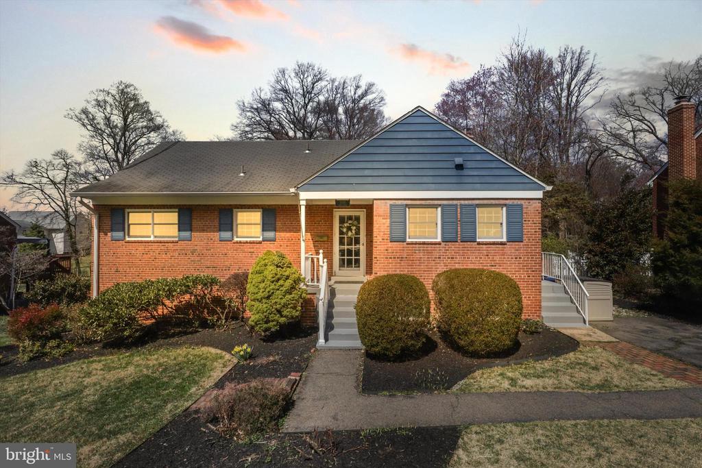 Brick ranch house with a blue gable, central entry steps, and trimmed front shrubs.