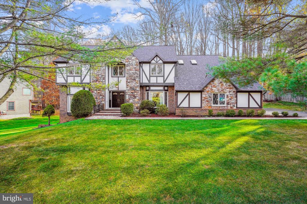Tudor-style house with stone facade, half-timbered siding, and a broad lawn.