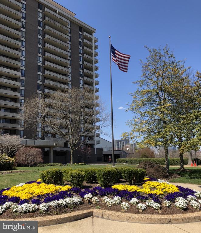 Multi-story building with a U.S. flag and colorful flower beds in front.