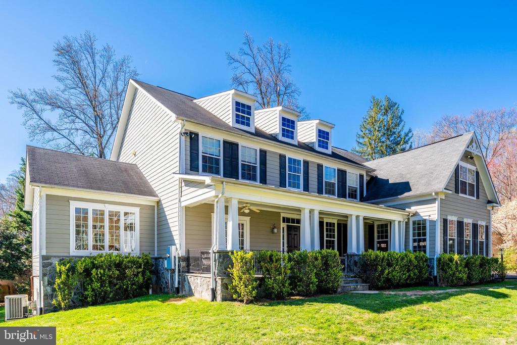 White-sided two-story house with dormer windows and a long covered front porch.