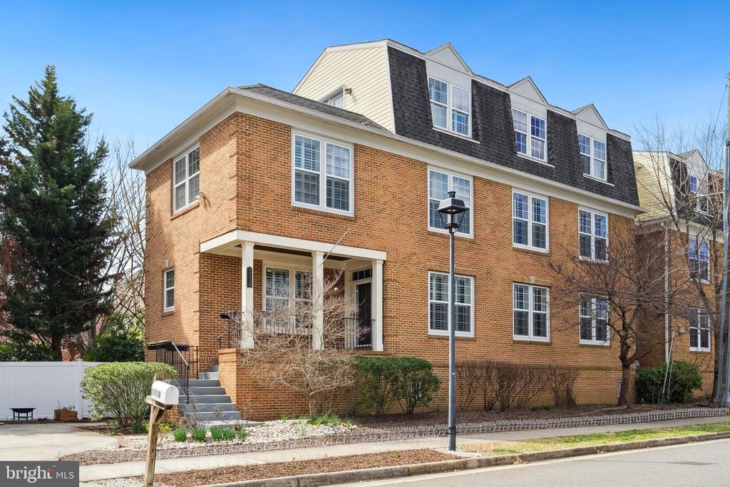 Brick home with a covered front porch, dark dormers, and steps beside the street.