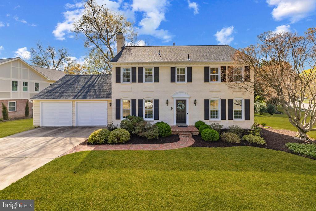 White brick two-story house with black shutters, double garage, and curved brick walkway.