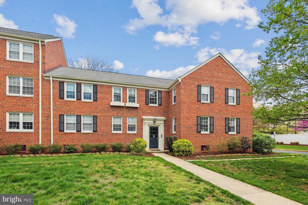 Red-brick multifamily building with a central entrance, landscaped shrubs, and a front lawn.