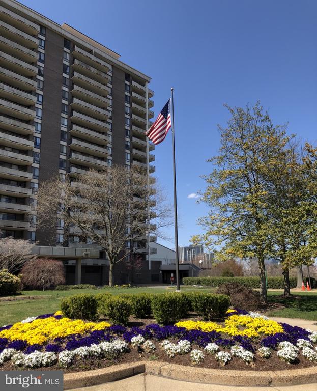 Condominium building with stacked balconies, an American flag, and colorful flower beds.