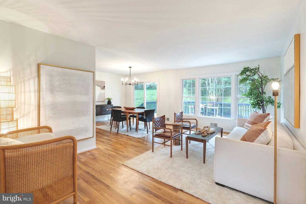 Open-plan living and dining room with hardwood floors, woven chairs, and large windows overlooking a yard.