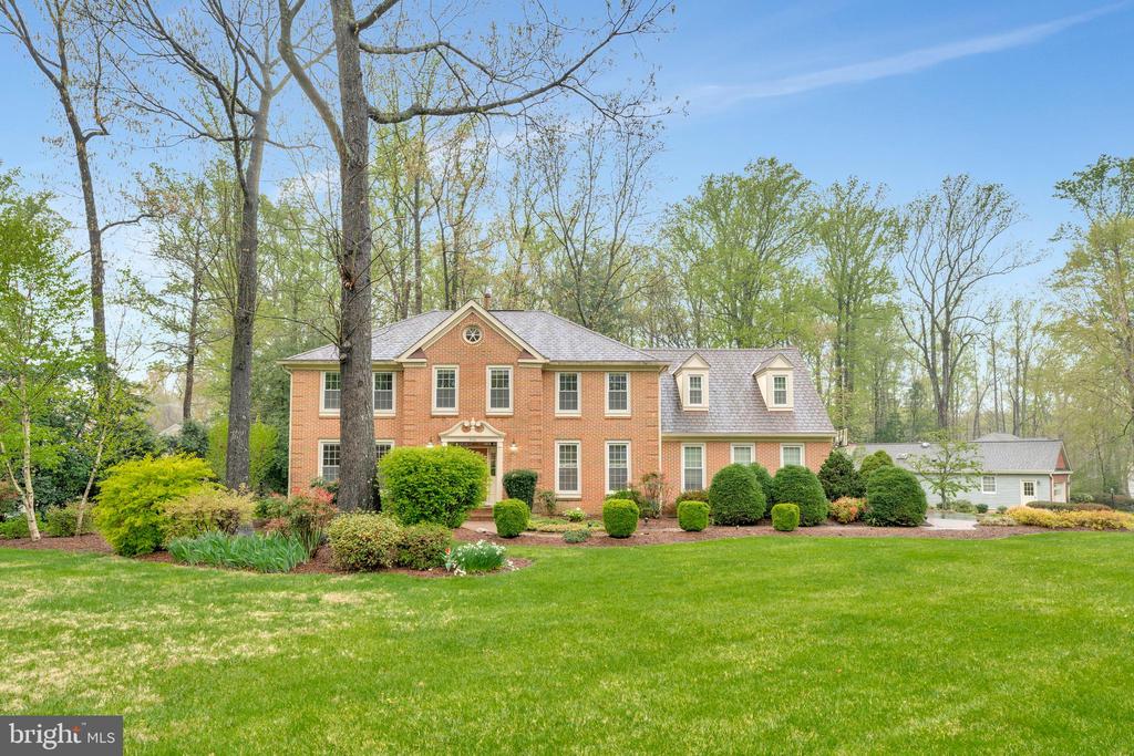 Two-story red-brick home with landscaped shrubs and a broad green lawn.