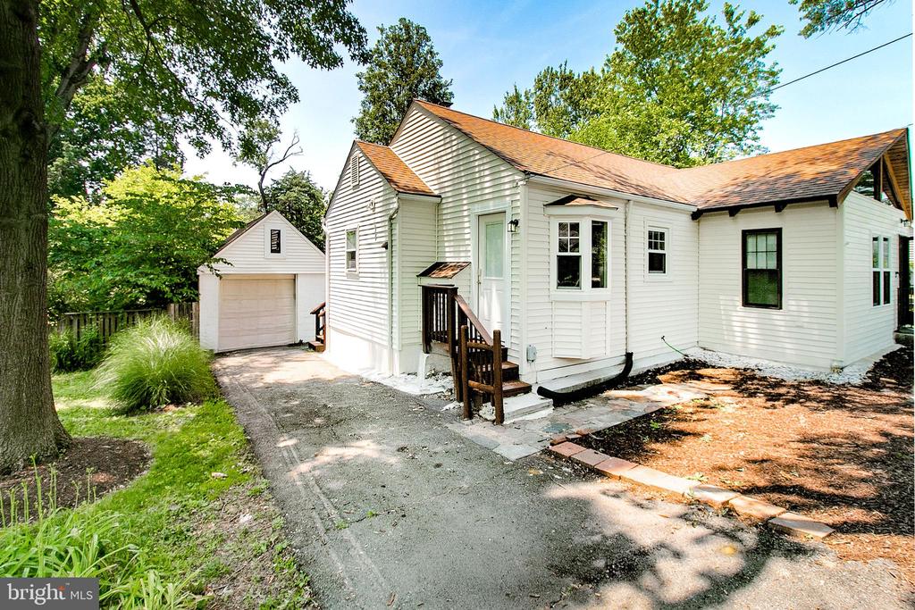 White single-story house with a detached garage, paved driveway, and mature trees.
