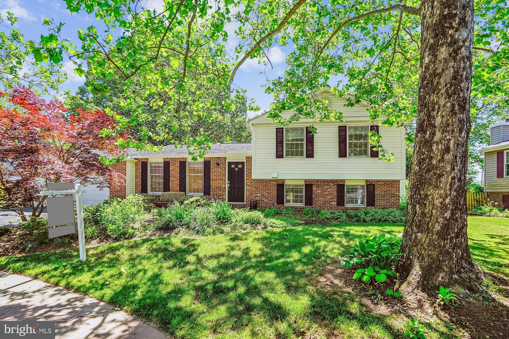 Split-level brick and white-sided home framed by mature trees and a landscaped lawn.