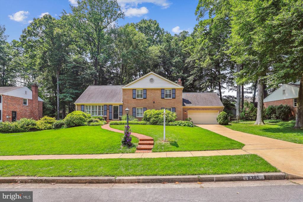 Two-story brick house with an attached garage, curved brick walkway, and mature trees.