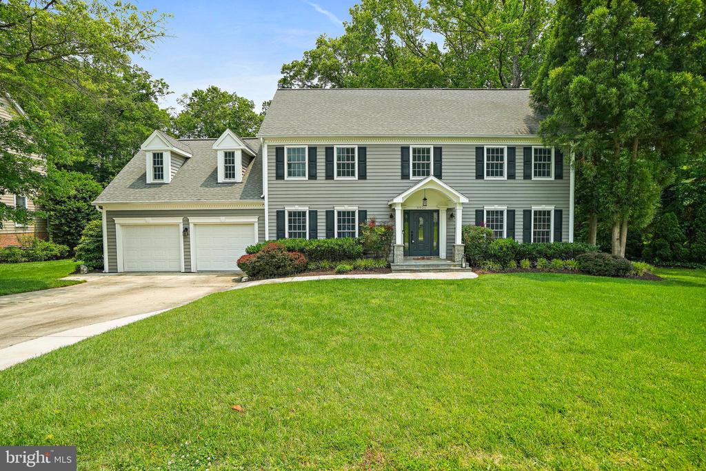 Gray two-story house with dark shutters, attached garage, and broad green lawn.