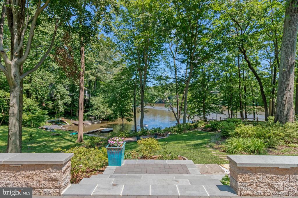 Landscaped riverfront yard with stone steps, mature trees, and a dock along the water.