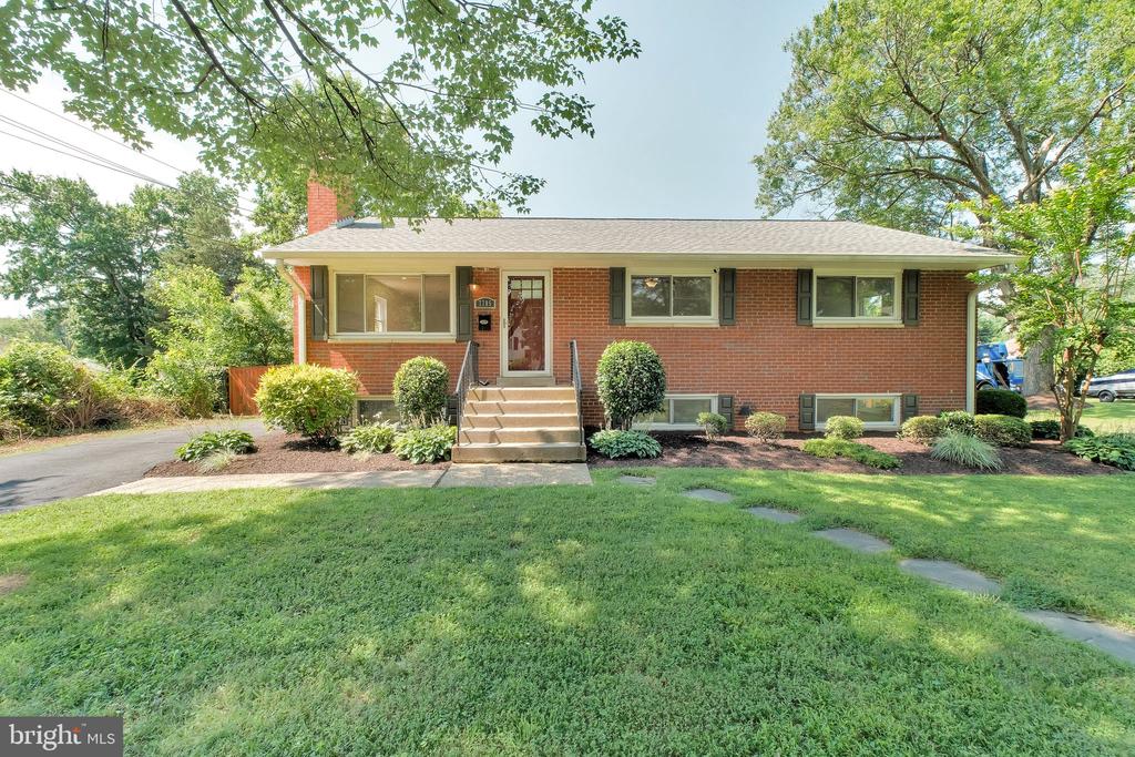 Single-story red brick house with front steps, basement windows, and a broad lawn beneath mature trees.