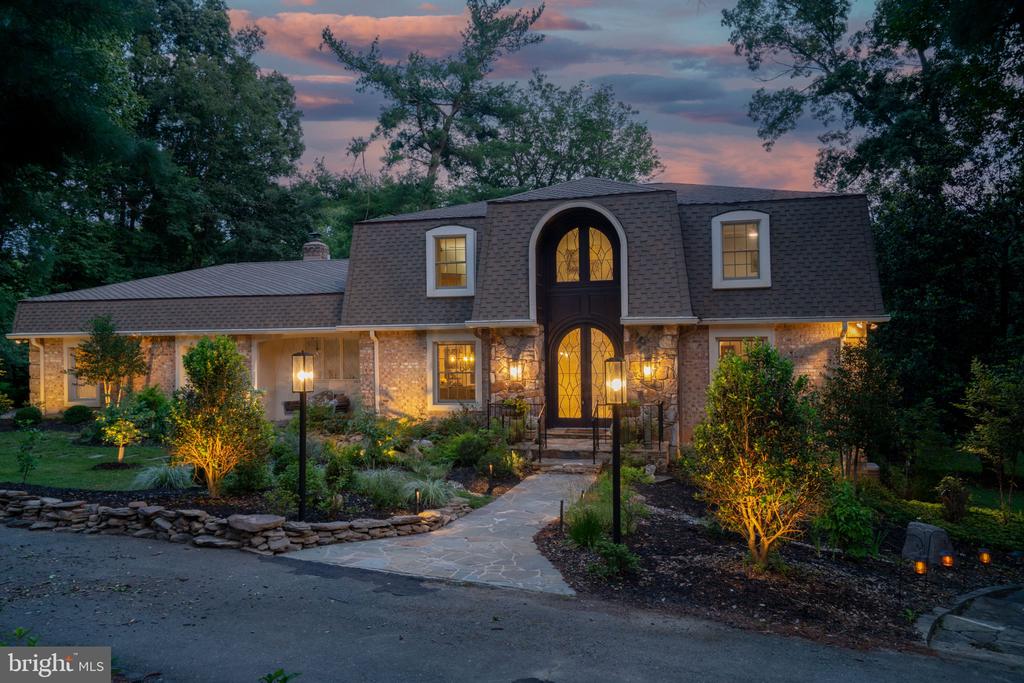 Brick and stone home with a tall arched entry and landscaped front garden at dusk.