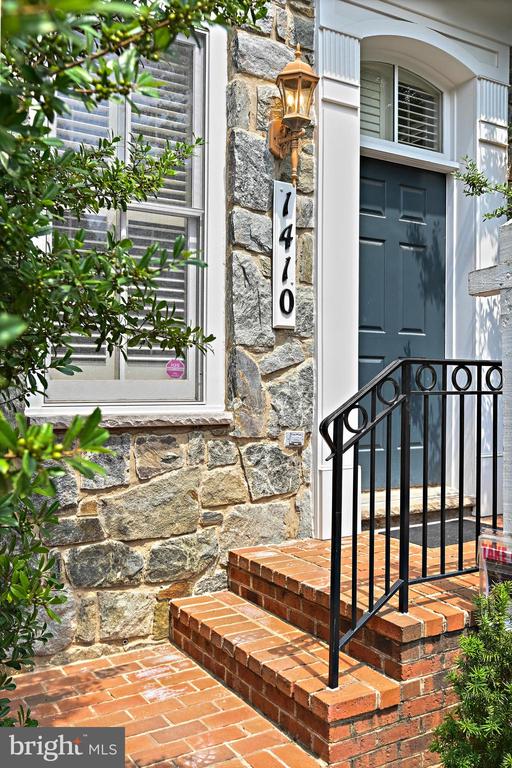 Stone home entrance with a dark blue door, brick steps, black railing, and house number 7410.