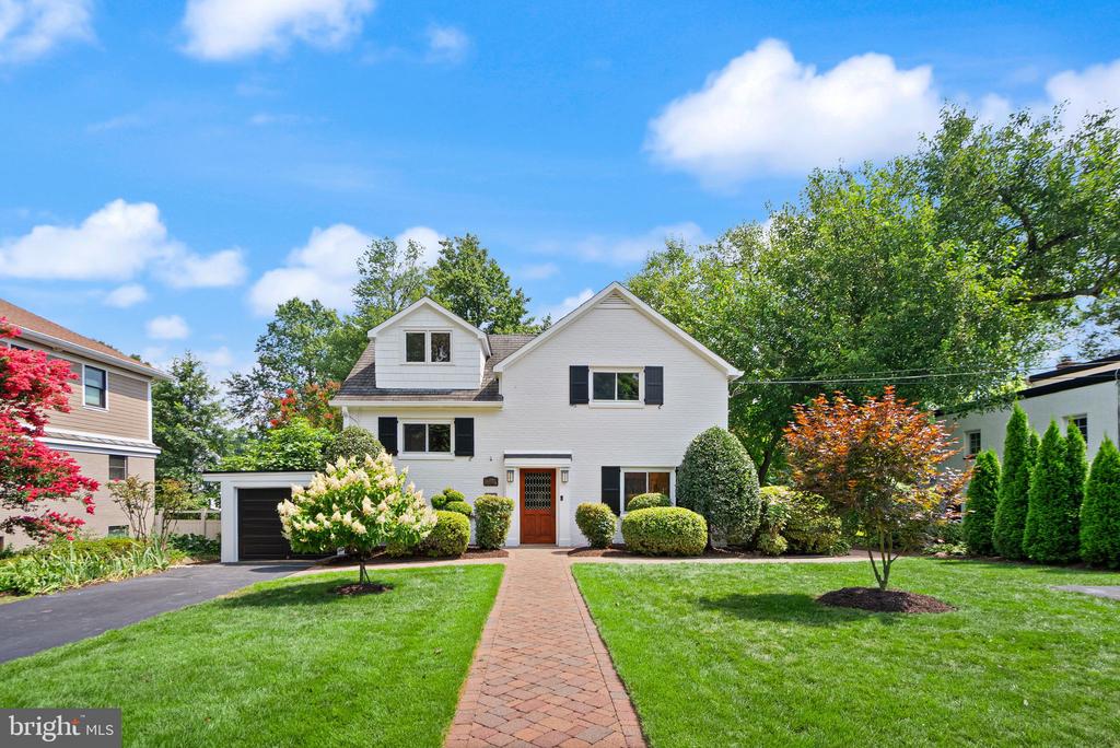 White two-story house with black shutters, attached garage, and brick walkway through a landscaped lawn.