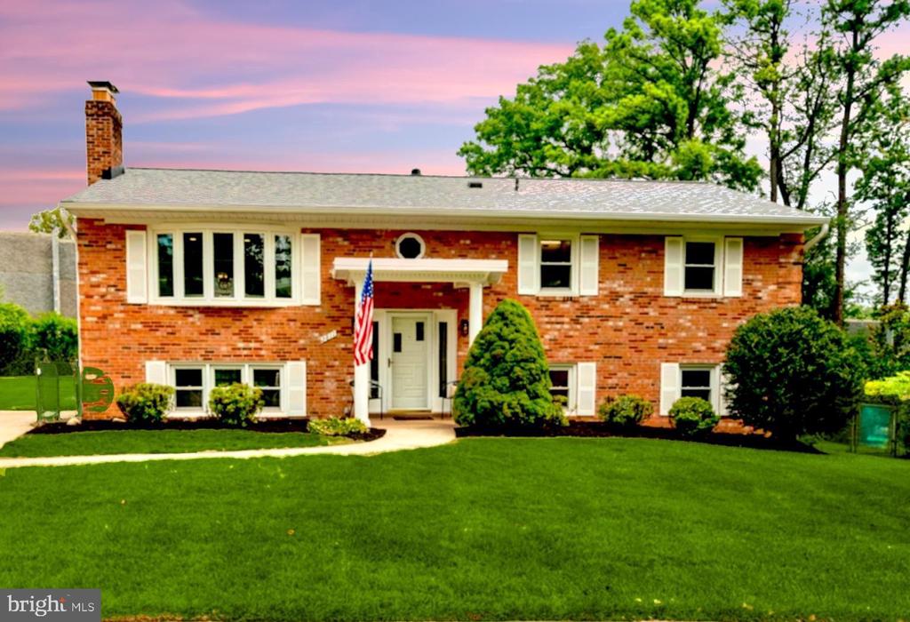 Red-brick split-level home with a white entrance canopy, American flag, and broad green lawn.
