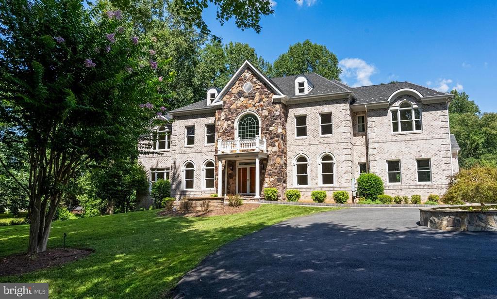 Large brick and stone house with arched windows, a landscaped lawn, and a paved driveway.