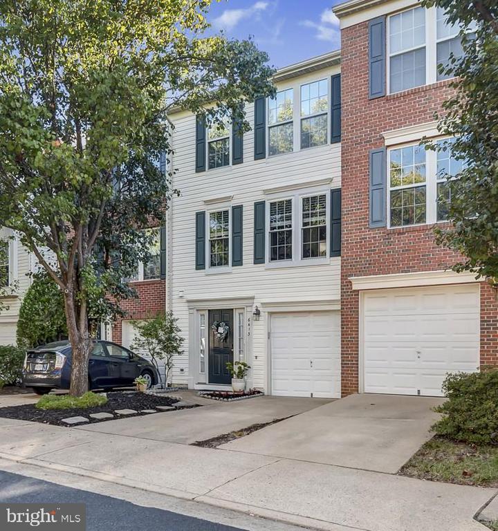 Attached townhouse with white siding, red brick sections, dark shutters, and two garage doors.
