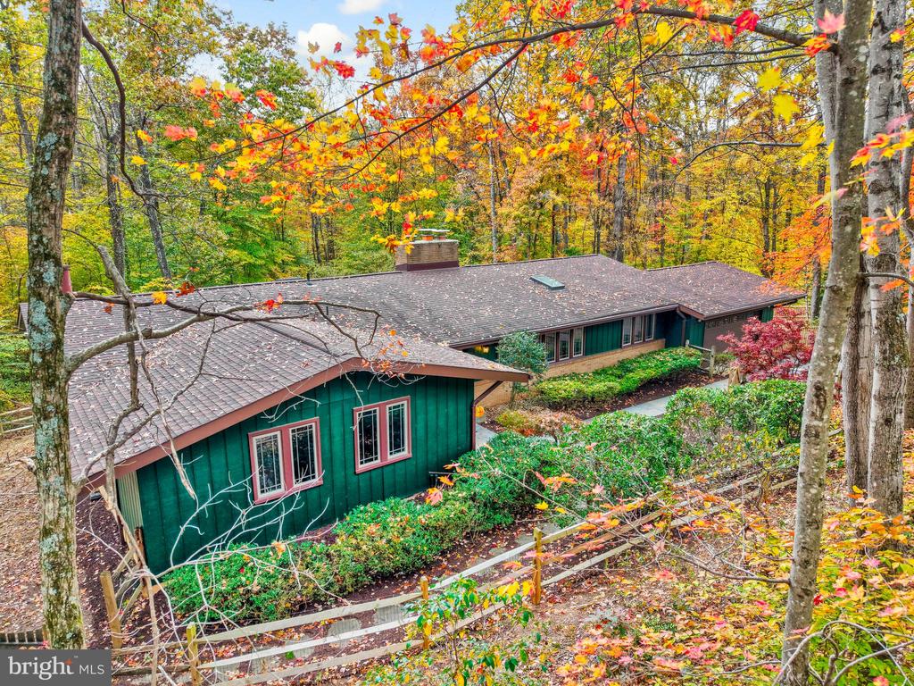 Green-sided house nestled among colorful autumn trees, viewed above its landscaped garden.