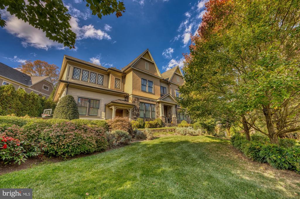 Two-story house with tan siding and stone accents, framed by autumn trees and landscaped grounds.