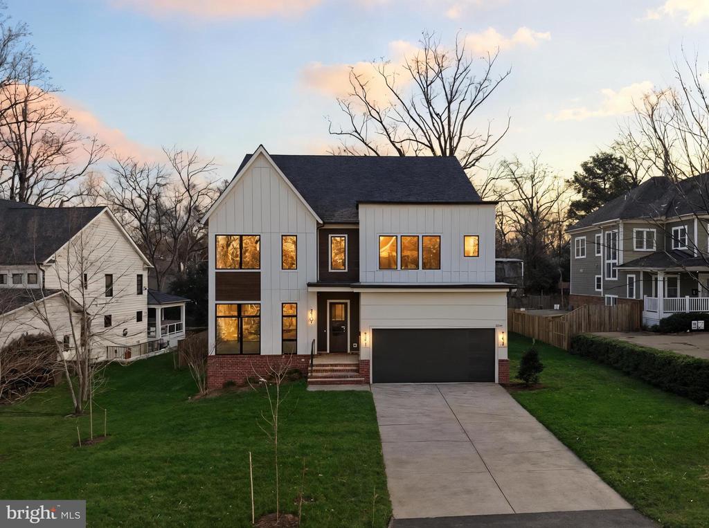 Modern white two-story house with an attached garage and wide driveway at dusk.