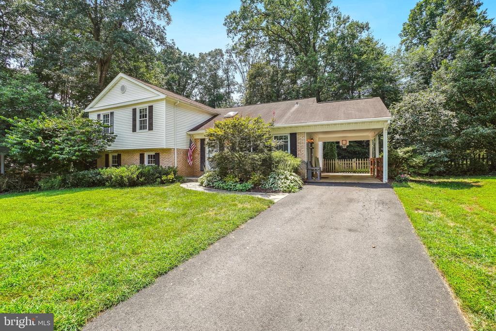 Split-level home with white siding, brick lower level, covered carport, and wide driveway.