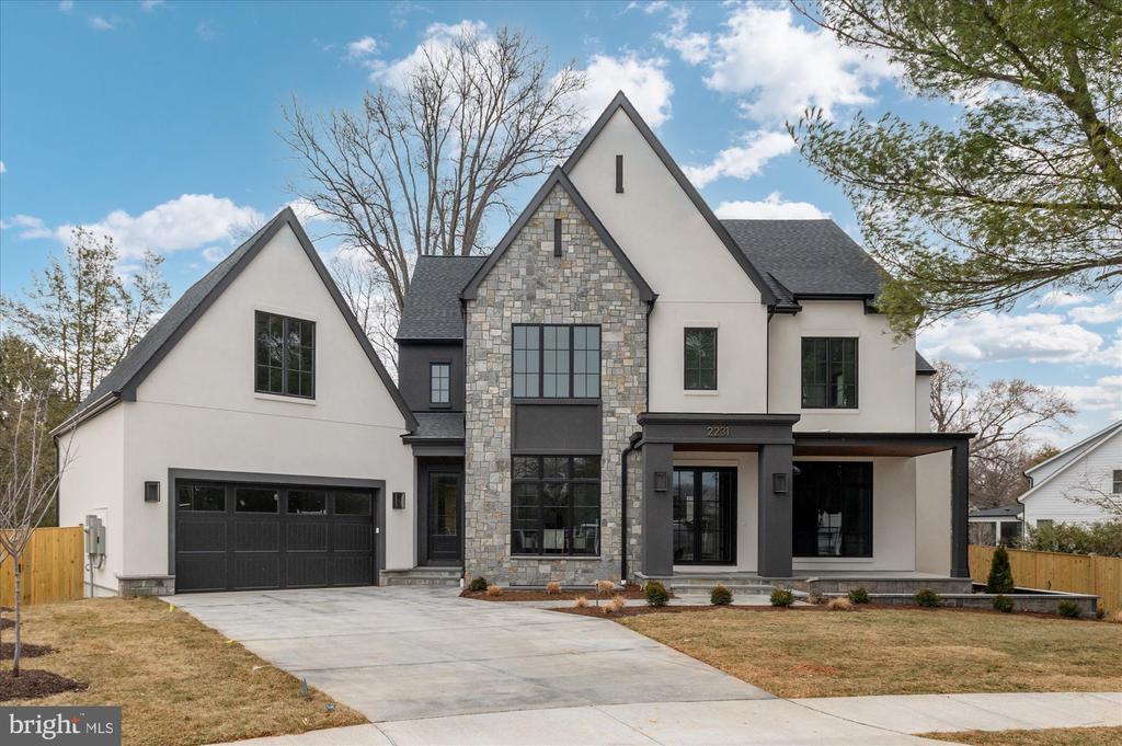 Modern two-story home with a central stone facade, steep gables, attached garage, and broad driveway.