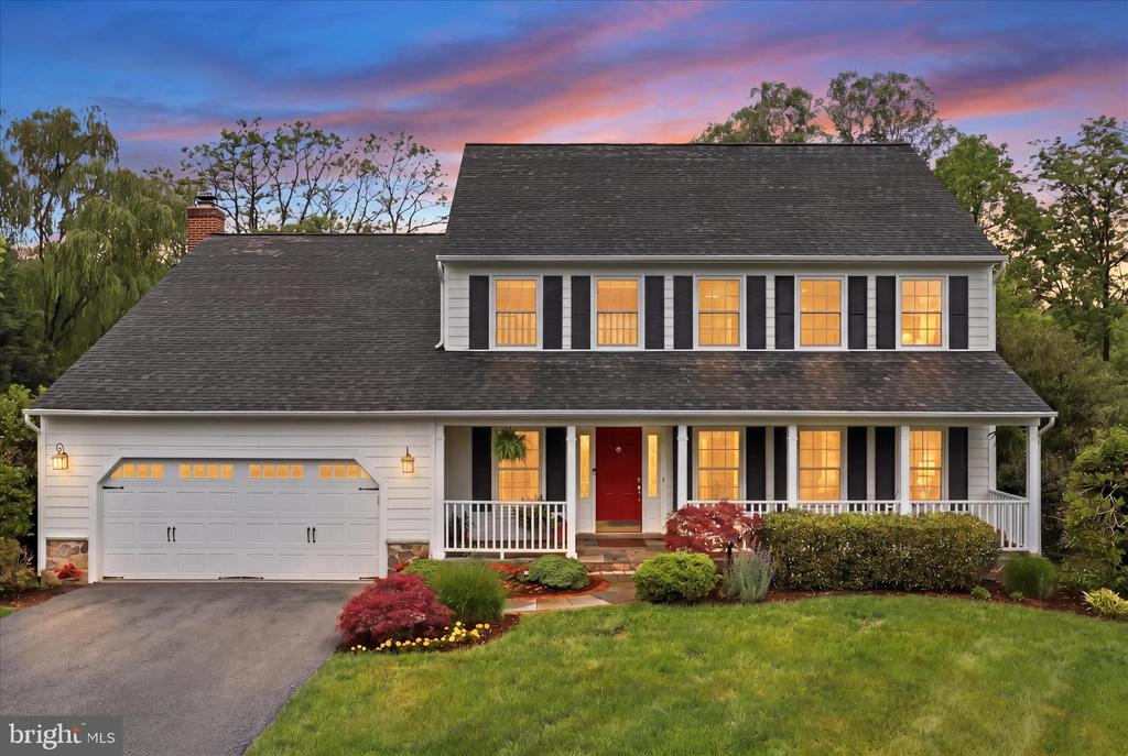 Two-story white house with black shutters, a red door, and a covered porch at dusk.