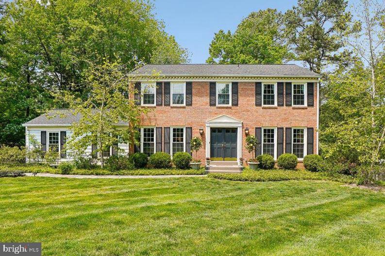 Two-story brick colonial home with black shutters, a side wing, and a broad green lawn.