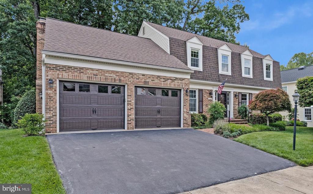 Two-story brick house with double garage, four dormers, and a wide paved driveway.