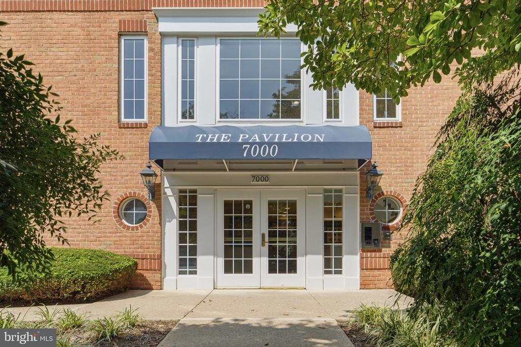 Brick building entrance marked The Pavilion 7000, with a blue canopy and white-framed glass doors.