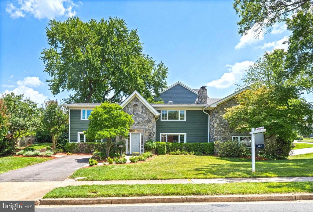 Two-story green home with stone accents, a landscaped lawn, and a real estate sign.